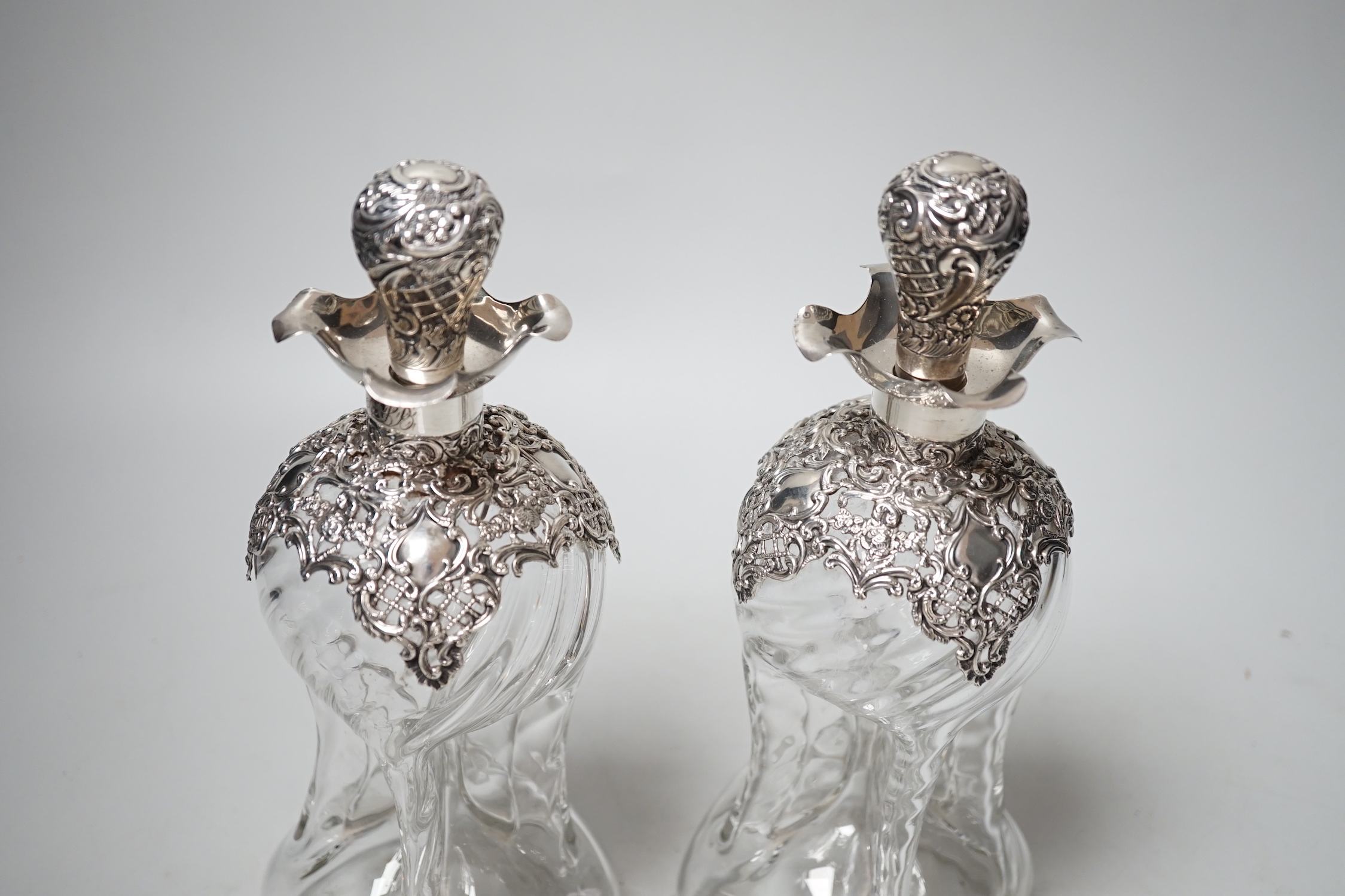 A pair of late Victorian repousse silver mounted hour glass decanters and stoppers, Henry Matthews, Birmingham, 1899, height 25mm.